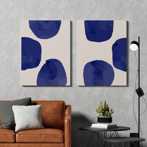 Two abstract art pieces with blue circles on a gray wall above a brown sofa.